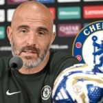 Enzo Maresca in a press conference with the Chelsea badge.